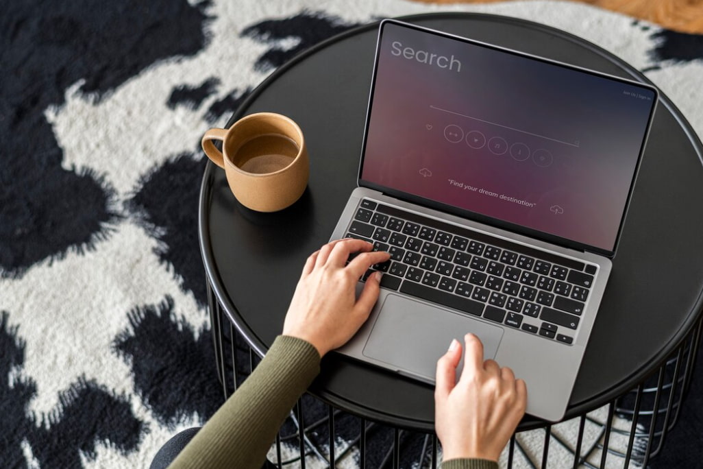 A person using a MacBook Pro on a black table next to a cup of coffee