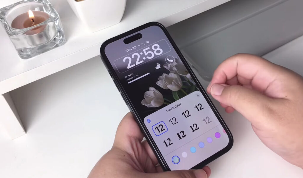 Hand holding iPhone with a floral lock screen and color-coded clock